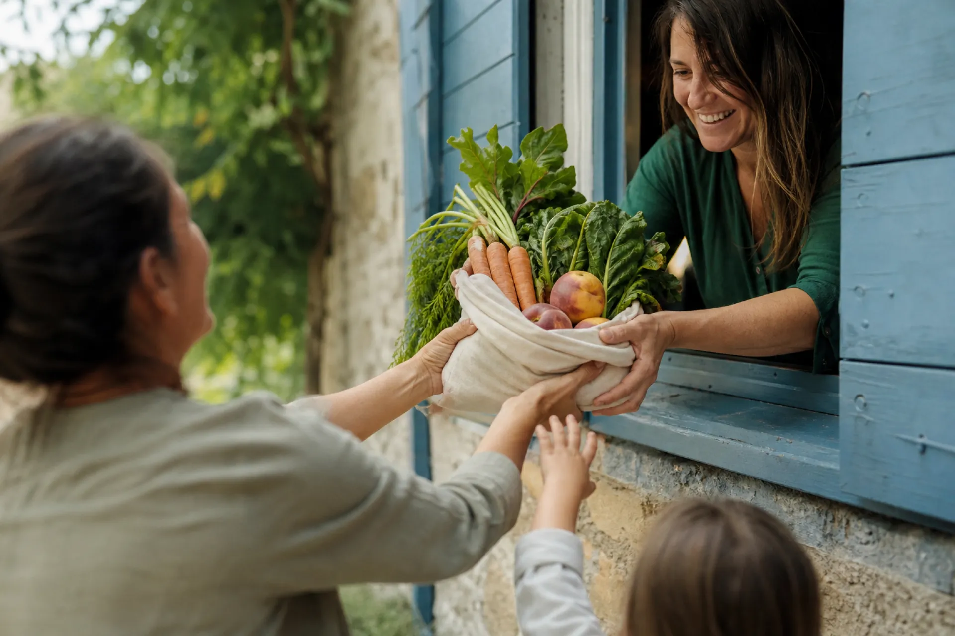 Mains de deux femmes se passant un sac en tissu de légumes et pêches bio par une fenêtre aux volets bleus, une main d'enfant tendue.